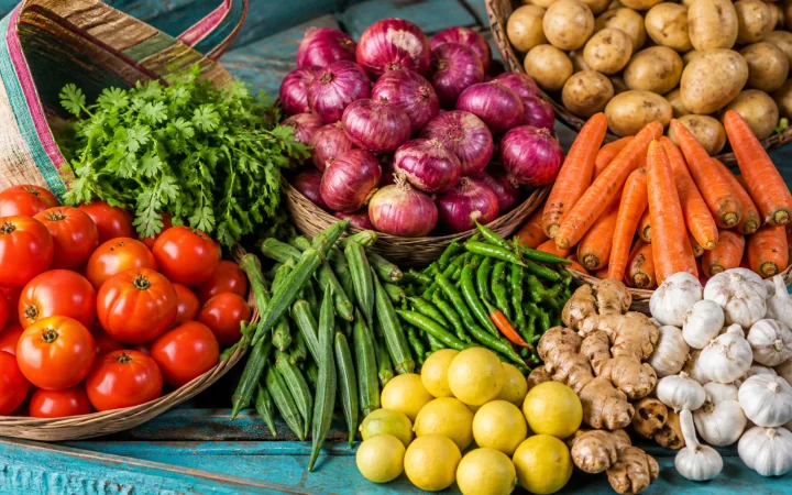 A colourful Indian market display of tomatoes, onions, potatoes, okra, chillies, carrots, lemons and herbs